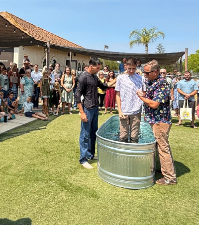 A baptism ceremony in a metal tub with a crowd watching, sunny day, three people involved.