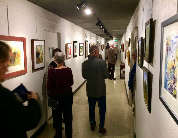 Art gallery corridor with several people viewing framed artwork on the walls.