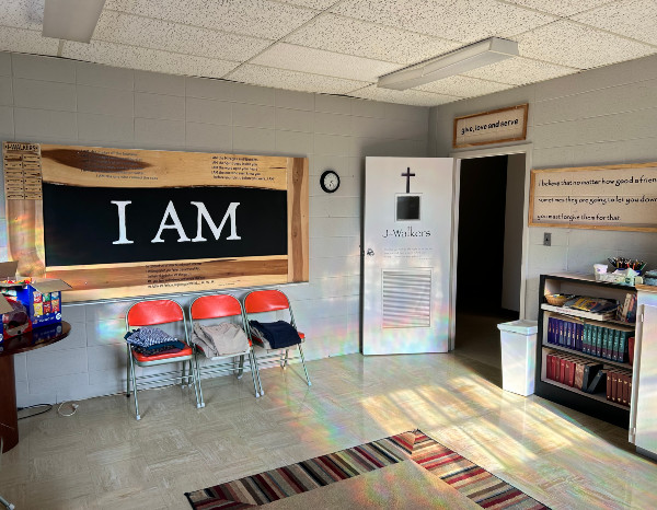 Classroom with "I AM" sign, red chairs, a clock, and a door labeled "J. Walkers," featuring inspirational text on the wall.