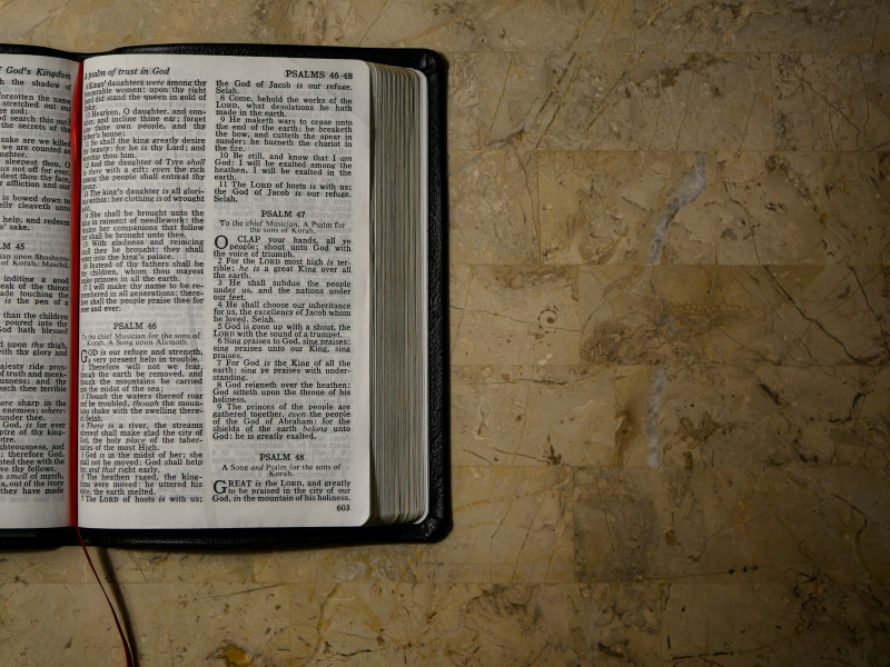 Open Bible on a marble surface, pages showing Psalms 46-48, with a red ribbon bookmark visible.