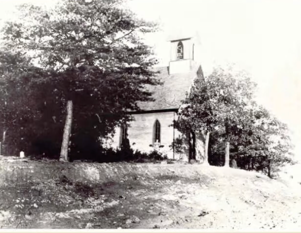 Historic church surrounded by trees, featuring a bell tower, captured in black and white. No visible date.