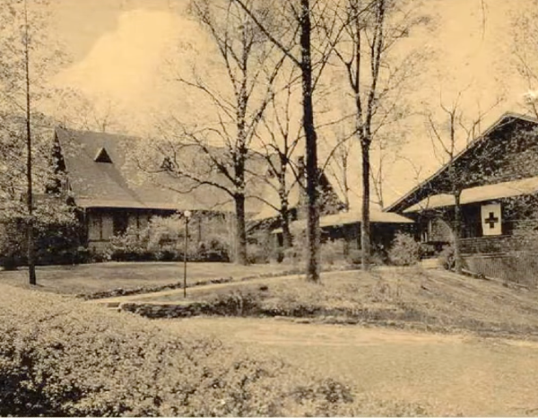 Historic black-and-white photo of two houses among trees, one with a red cross symbol on the side.