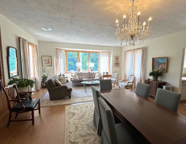 A bright living room with a chandelier, large windows, a dining table, and comfortable seating.
