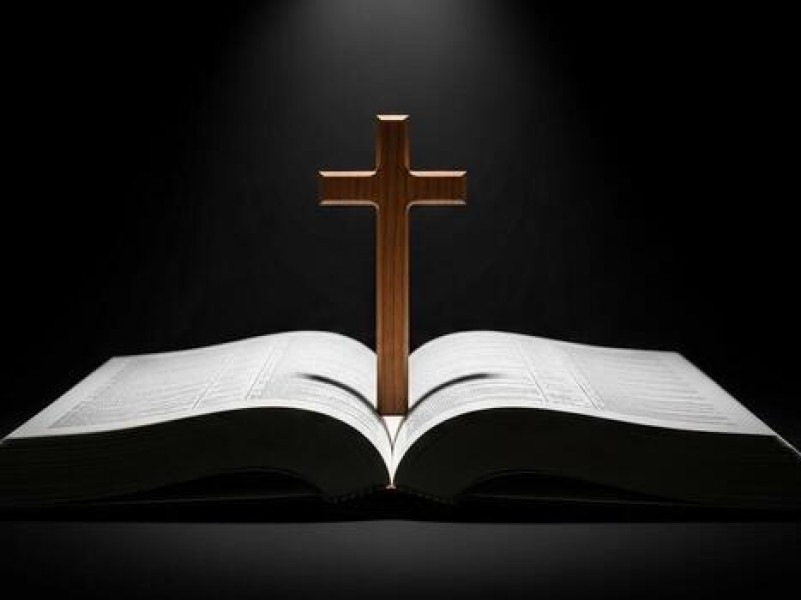 A wooden cross rests on an open Bible, illuminated against a dark background.