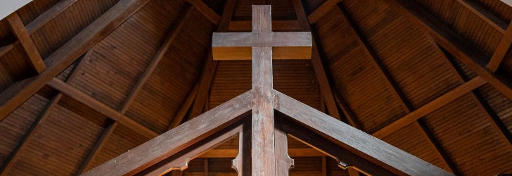 Wooden cross at the peak of a church ceiling with a wooden beam structure.